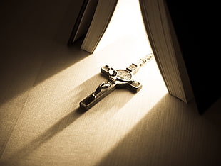silver-colored crucifix pendant near book